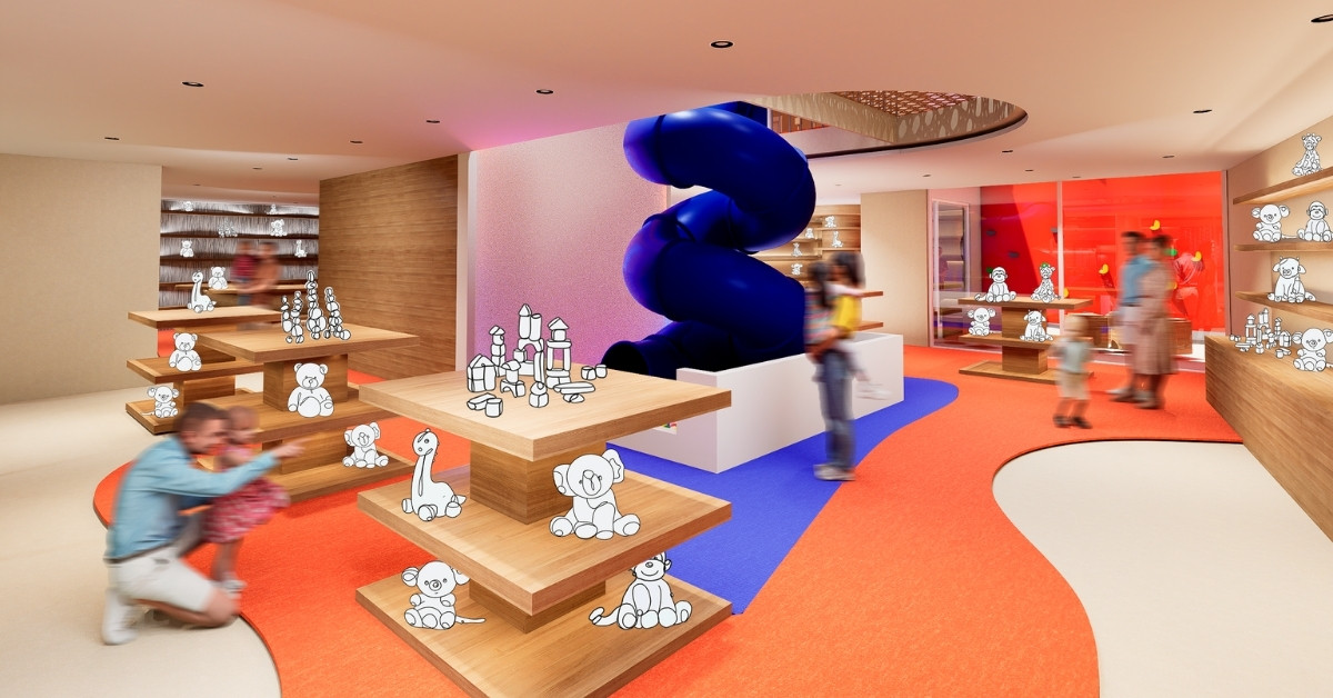 Vista interior de la planta baja de Ludoland, con un tobogán azul central de doble altura, estanterías de juguetes y suelo ondulado en colores rojo y azul.